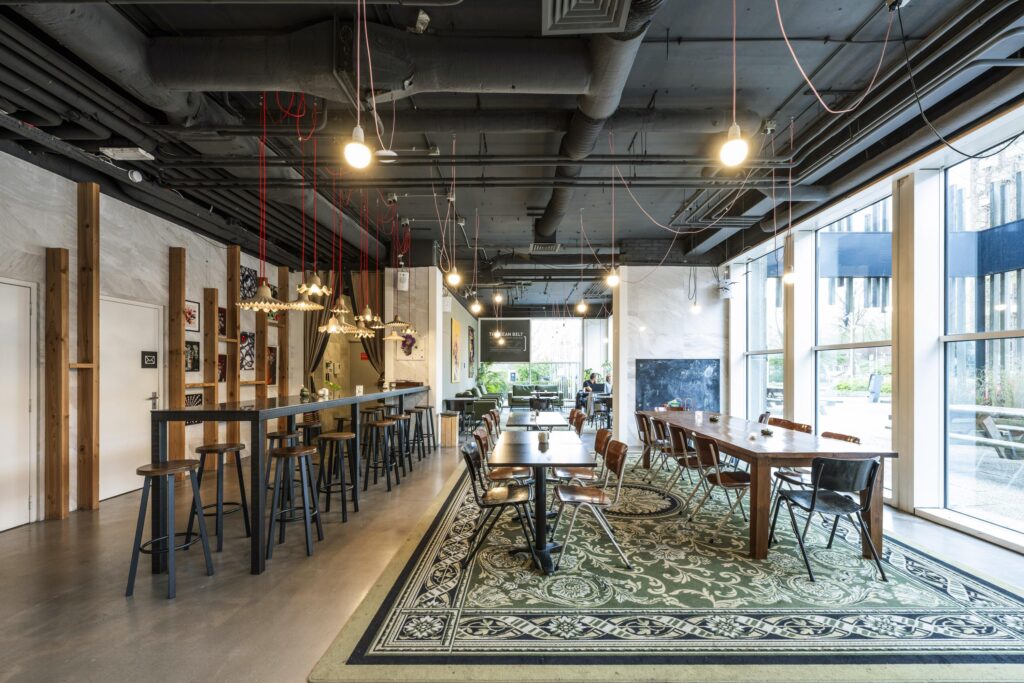 Modern coworking space at Laan van Kronenburg with long communal tables, high stools, and large windows providing natural light.